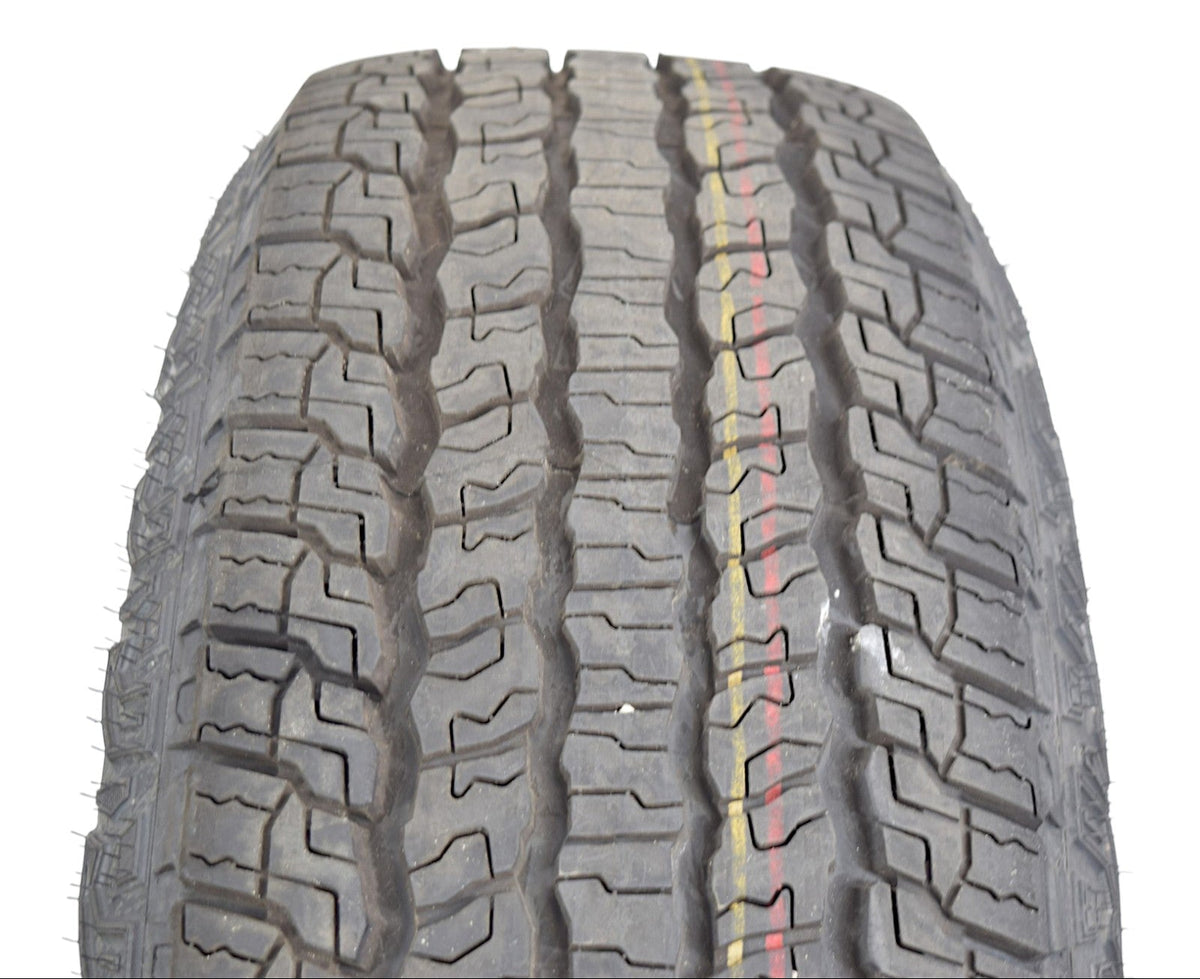 A close-up of a rugged all-terrain tire tread pattern, showing the detailed grooves and a thin yellow and red center stripe, isolated on a white background.