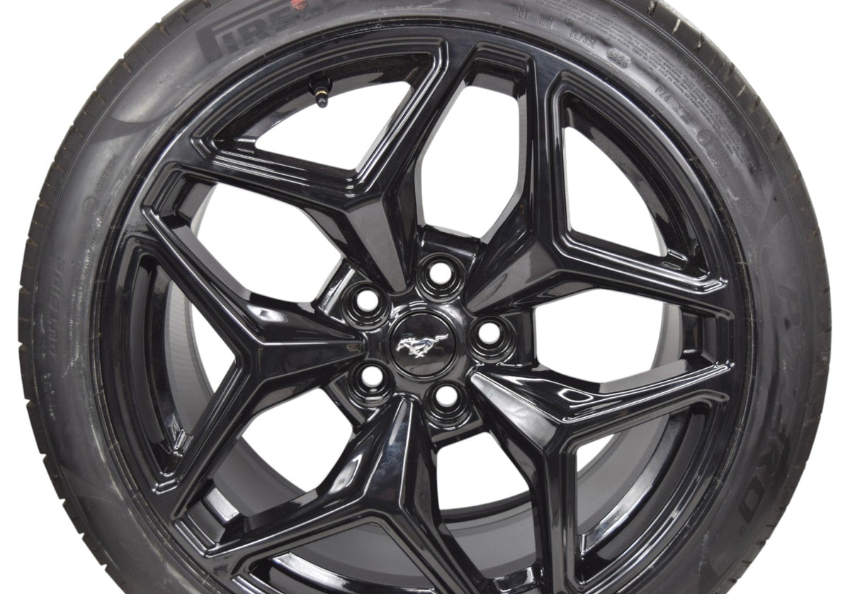 A close-up of a black multi-spoke alloy wheel with a black tire, featuring a Mustang logo in the center, set against a plain white background.