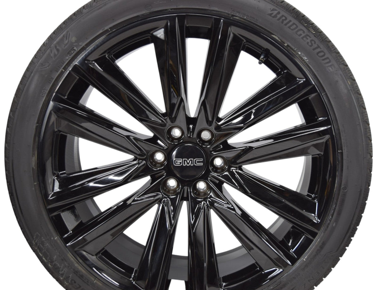 A glossy black multi-spoke alloy wheel with a Bridgestone tire mounted on it, featuring a central GMC logo badge.
