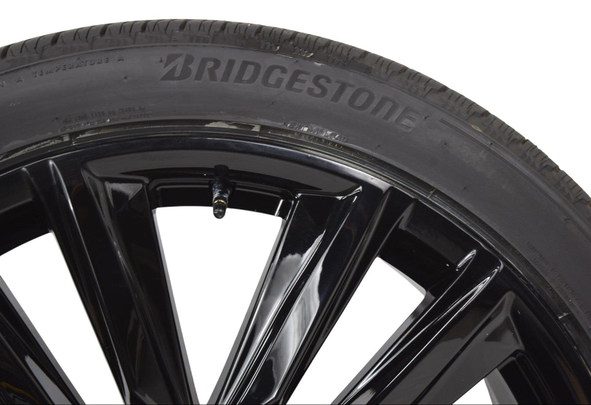 Close-up of a black Bridgestone tire mounted on a glossy black multi-spoke alloy wheel, shown against a solid white background.