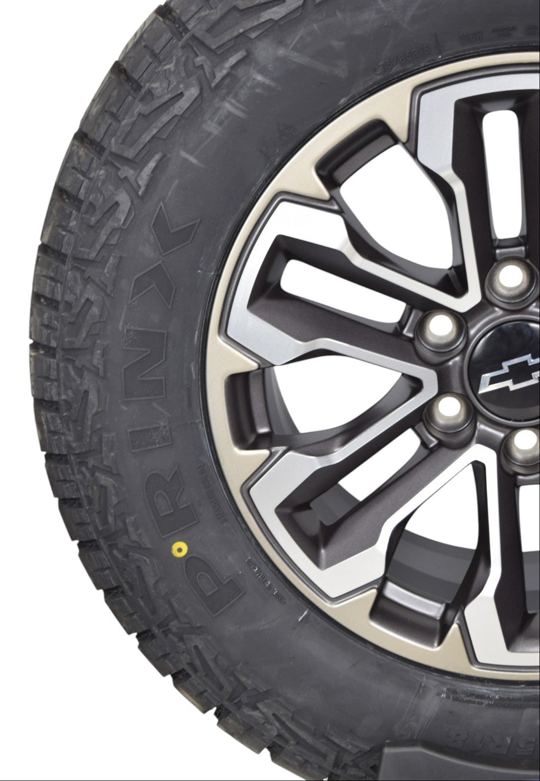 Close-up of a black off-road tire with visible PRINX lettering, mounted on a multi-spoke silver and black alloy wheel with a Chevrolet logo center cap, isolated on a white background.