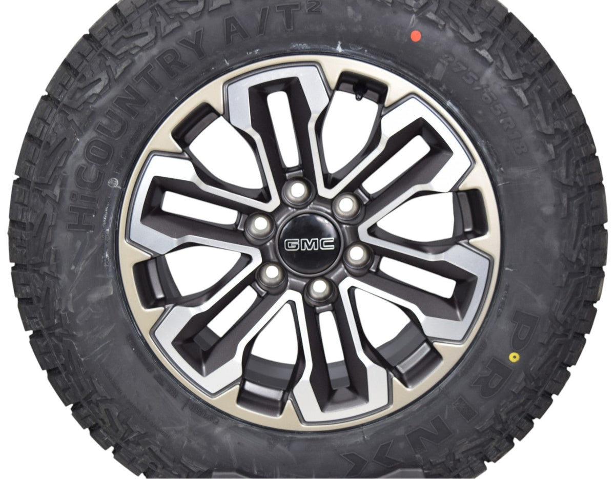 A rugged off-road tire mounted on a multi-spoke silver and black alloy wheel with a central GMC logo, isolated on a white background.